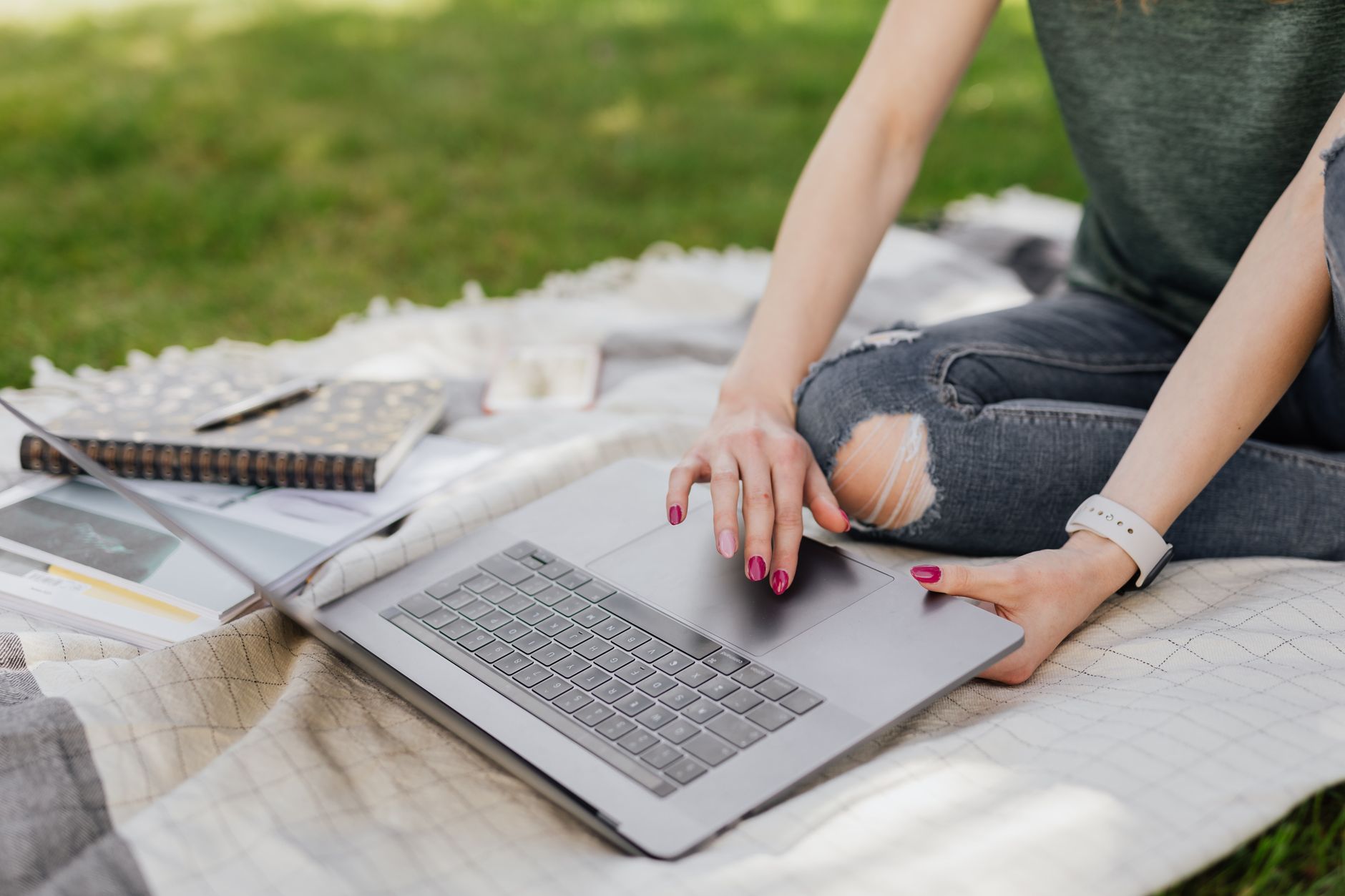 Étudiante non reconnaissable faisant des recherches sur Internet sur un ordinateur portable assise sur une couverture confortable dans un parc verdoyant en été par une journée ensoleillée