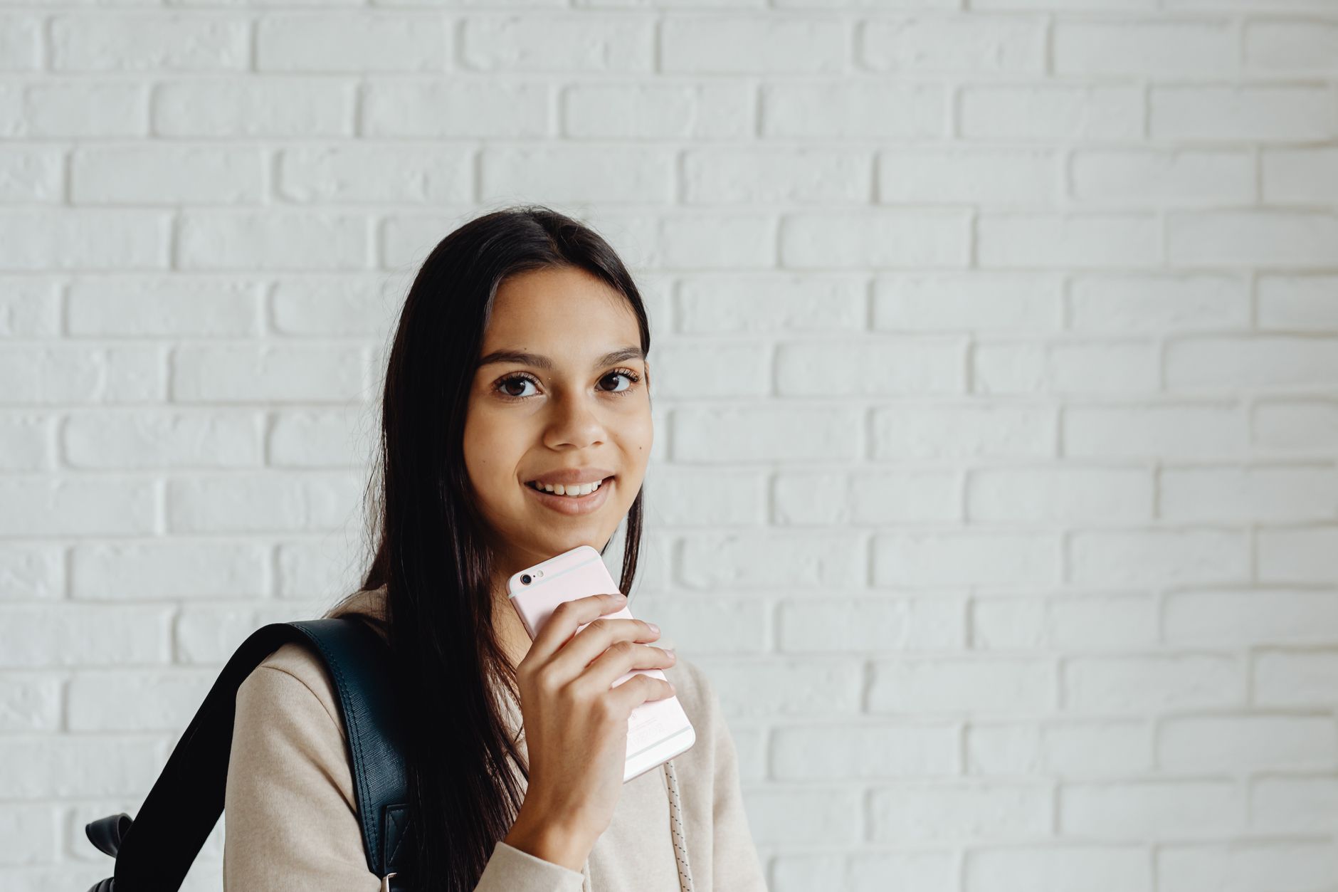 Une jeune femme aux cheveux noirs tient un smartphone en souriant à l'intérieur.