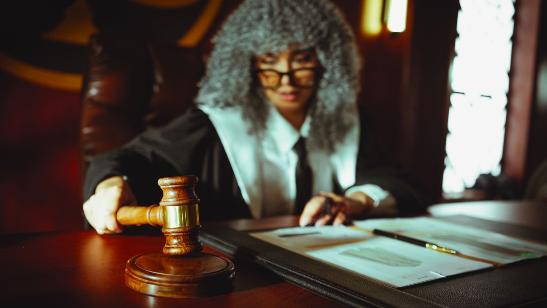 Juge féminin dans une salle d'audience, se concentrant sur des documents juridiques avec un maillet.